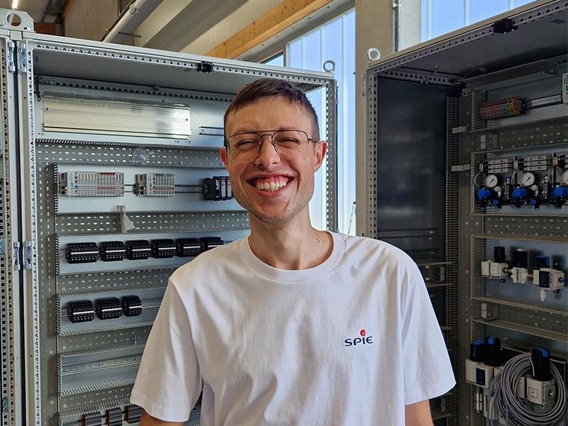Apprentice Leon grins into the camera. In the background is a control cabinet